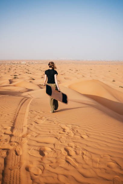 Female tourist walking with a sandboard in the Dubai desert