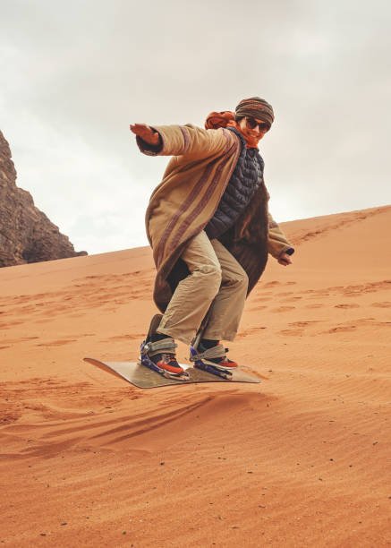 Young woman posing as sand dune surfing wearing bisht - traditional Bedouin coat. 