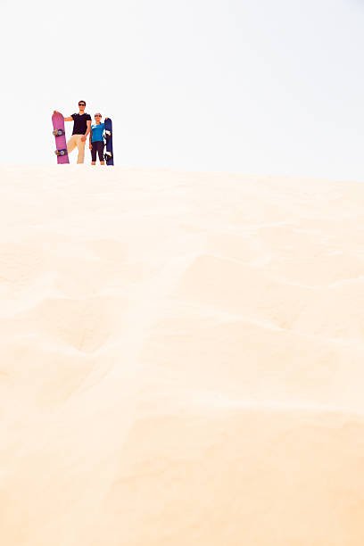 tourists standing at the top of a dune, getting ready for some sandboarding fun