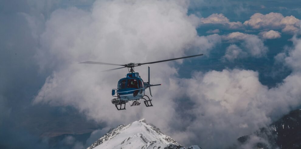 A helicopter soaring over Dubai's mountain range with clouds in the background.