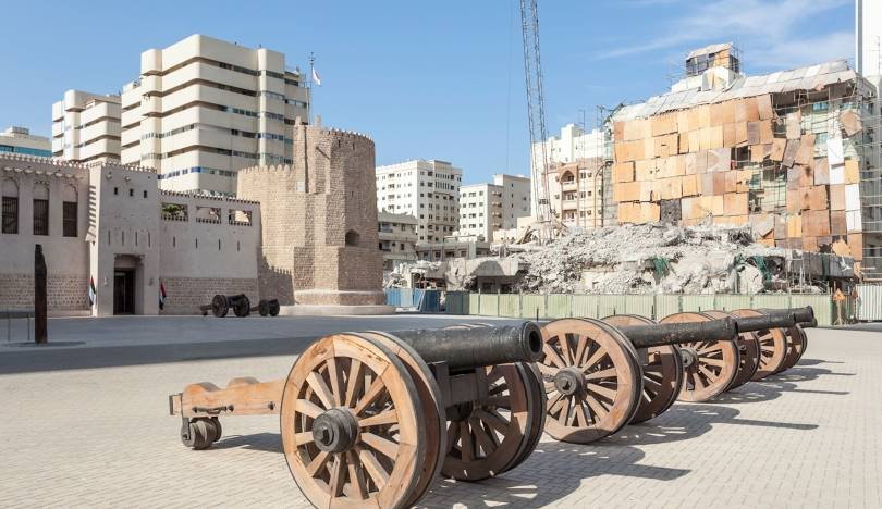 Old cannons outside Al Hisn Fort, surrounded by city buildings.