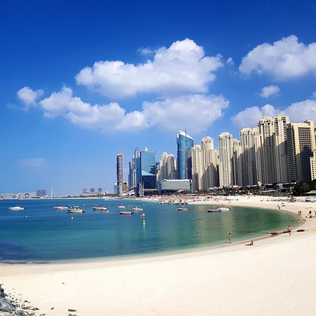 A sandy beach with a city skyline in the background, Dubai Marina Beach.