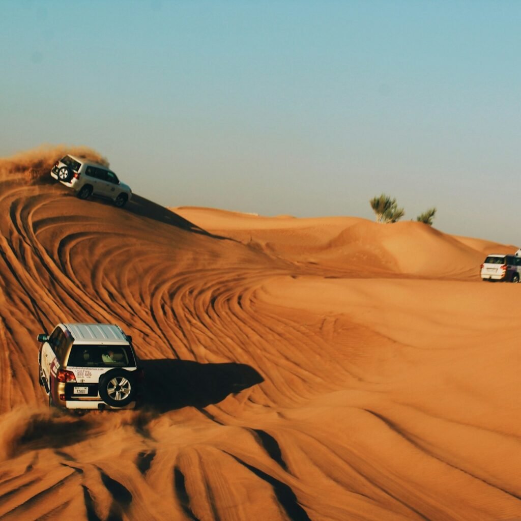 Desert adventure in Dubai: Four jeeps driving through the sandy dunes on a sunny day.