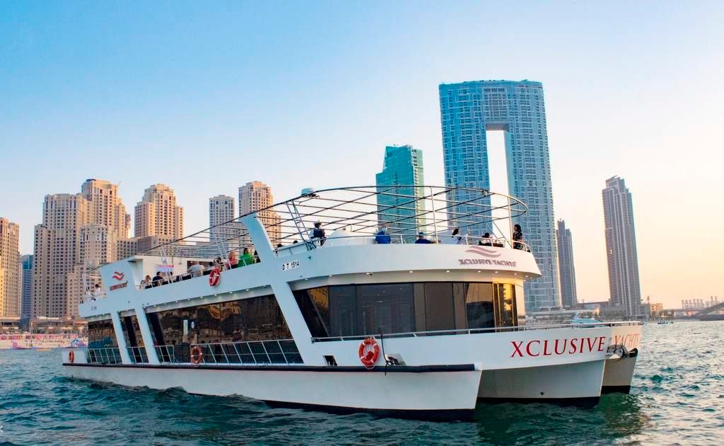 A scenic view of a boat with people on board navigating through Dubai Marina.