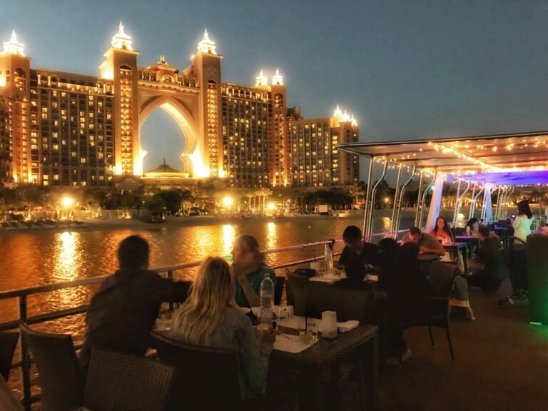 People dining at tables on the water in front of Atlantis Hotel, Palm Jumeirah Yacht Cruises.