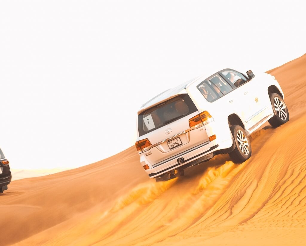 Two vehicles driving through the desert on a sand dune.