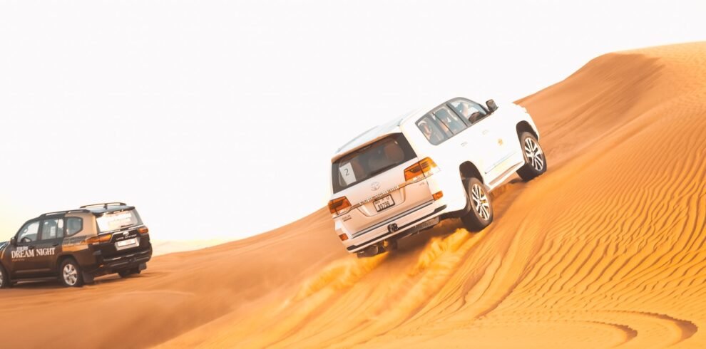 Two vehicles driving through the desert on a sand dune.