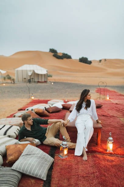 Stylish european couple in love enjoying evening together in luxury glamping camp. Romantic mood, lying on multicolor pillows.