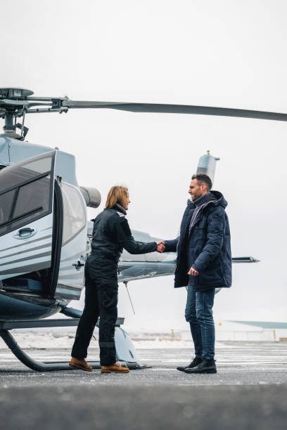 Chopper pilot welcoming a male passenger on helipad. Pilot greeting man with handshake by the helicopter.