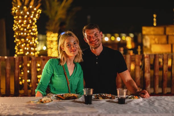 Portrait of a young adult Caucasian tourists hugging and smiling at the camera at dinner in a safari camp in Dubai.