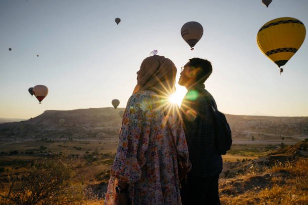 young muslim couple enjoy the sunrise with view of  hot balloon in goreme