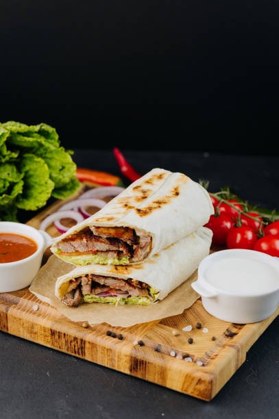 Tasty beef shawarma with fresh salad and vegetables lying on wooden board. Traditional arab dishes