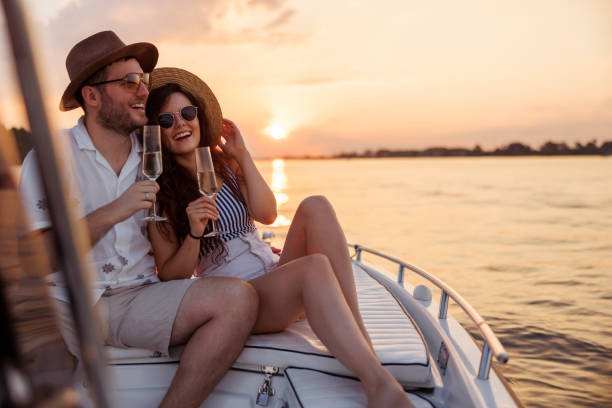 Couple in love enjoying summer vacation, hugging and drinking champagne while sailing to the sunset on a boat