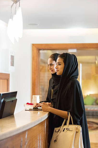 iStockalypse Dubai.  Closeup of two Emirati, Arabian girlfriends wearing black abaya and waiting to check in to a spa at a luxurious hotel spa resort.  Lobby in the background.  Dubai, UAE, Middle East, GCC.